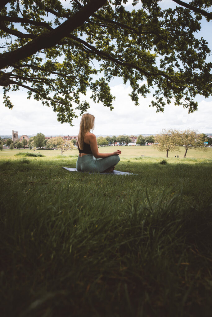 woman meditating under the tree sitting on grass